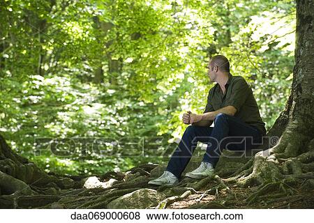 Stock Photo - Man sitting on tree roots in woods. Fotosearch