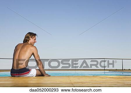 Stock Image - Man sitting poolside, dipping feet in water. Fotosearch