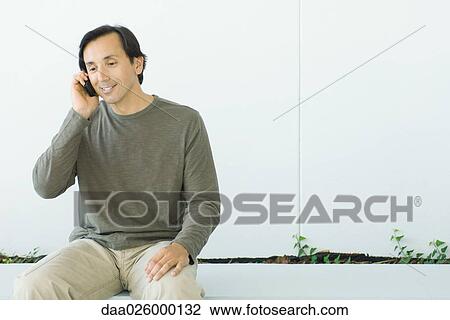 Man sitting, using cell phone, smiling, looking down View Large Photo Image Stock Image - Man sitting, using cell phone, smiling, looking down. Fotosearch