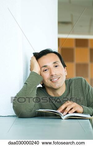 Man sitting with book, holding head, smiling at camera View Large Photo Image Stock Image - Man sitting with book, holding head, smiling at camera. Fotosearch