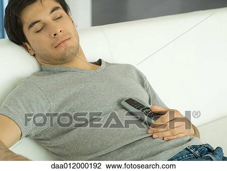 Stock Image - Man sleeping on sofa with remote control on chest. Fotosearch