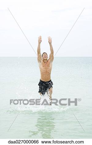 Stock Photograph - Man splashing in water, arms raised, head back. Fotosearch