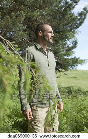 Stock Photograph - Man standing beside tree, looking at view. Fotosearch