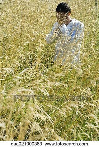 Stock Image - Man standing in field, covering face. Fotosearch