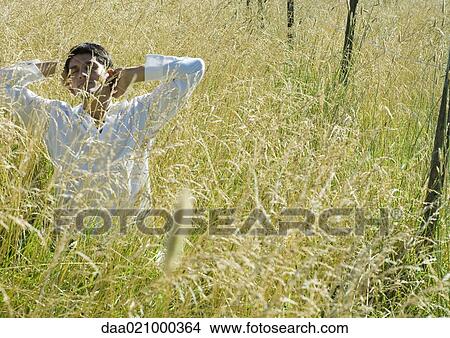 Man standing in field, hands behind head View Large Photo Image Picture - Man standing in field, hands behind head. Fotosearch