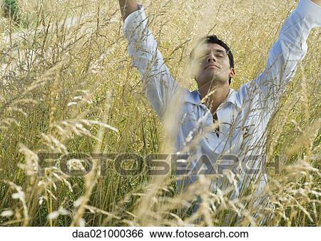 Man standing in field, raising arms, eyes closed View Large Photo Image Stock Photograph - Man standing in field, raising arms, eyes closed. Fotosearch