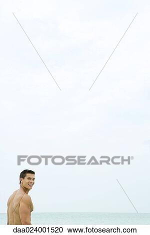 Man standing in front of ocean, smiling over shoulder at camera View Large Photo Image Stock Image - Man standing in front of ocean, smiling over shoulder at camera. Fotosearch