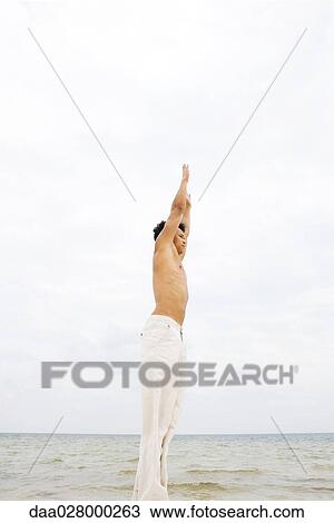 Man standing in front of ocean, stretching arms overhead, side view View Large Photo Image Stock Image - Man standing in front of ocean, stretching arms overhead, side view. Fotosearch