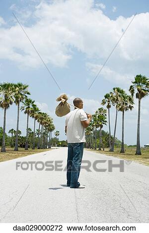 Man standing in middle of road, carrying burlap bundle on shoulder, rear view View Large Photo Image Stock Image - Man standing in middle of road, carrying burlap bundle on shoulder, rear view. Fotosearch
