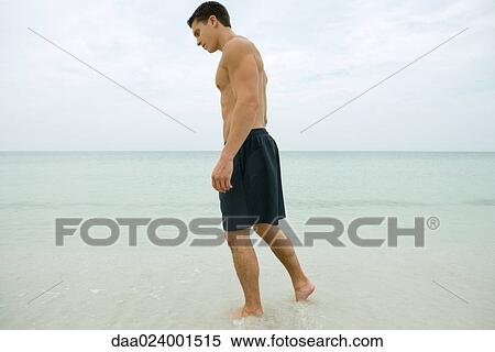 Stock Photography - Man standing in surf, full length. Fotosearch