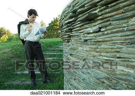 Man standing near stone wall, holding blueprints View Large Photo Image Picture - Man standing near stone wall, holding blueprints. Fotosearch