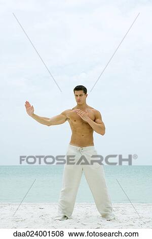 Man standing on beach, doing tai chi, full length View Large Photo Image Stock Photo - Man standing on beach, doing tai chi, full length. Fotosearch