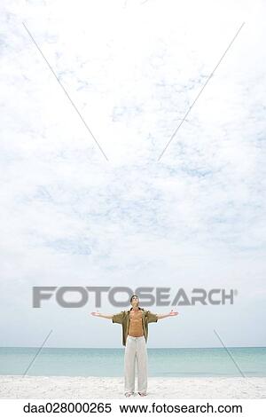 Stock Photography - Man standing on beach with head back and arms out, looking up at sky. Fotosearch