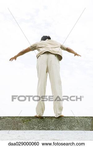 Man standing on ledge with arms out, leaning forward, rear view View Large Photo Image Stock Image - Man standing on ledge with arms out, leaning forward, rear view. Fotosearch