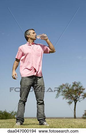 Man standing outdoors drinking from bottle of water, low angle view, full length View Large Photo Image Picture - Man standing outdoors drinking from bottle of water, low angle view, full length. Fotosearch