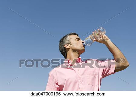Man standing outdoors drinking from bottle of water, low angle view, blue sky in background View Large Photo Image Stock Photograph - Man standing outdoors drinking from bottle of water, low angle view, blue sky in background. Fotosearch