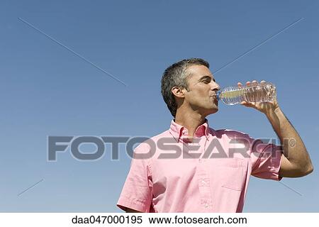 Man standing outdoors drinking from bottle of water, low angle view, blue sky in background View Large Photo Image Stock Photography - Man standing outdoors drinking from bottle of water, low angle view, blue sky in background. Fotosearch