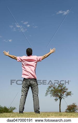 Stock Image - Man standing outdoors with arms raised, full length, rear view. Fotosearch