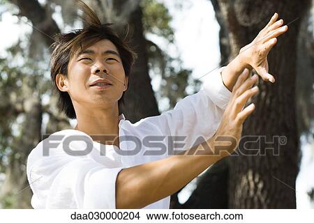 Picture - Man standing outdoors with hands raised, hair tousled by breeze, low angle view. Fotosearch