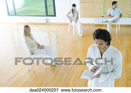 Stock Photo - Man standing reading book during group therapy session. Fotosearch