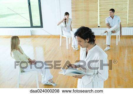 Man standing reading book during group therapy session View Large Photo Image Stock Photo - Man standing reading book during group therapy session. Fotosearch