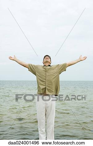 Man standing with head back and arms out, in front of ocean View Large Photo Image Stock Photograph - Man standing with head back and arms out, in front of ocean. Fotosearch