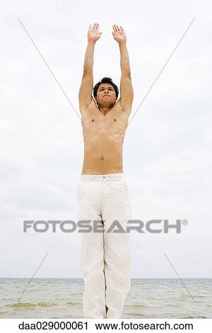 Stock Image - Man stretching at the beach, arms raised. Fotosearch