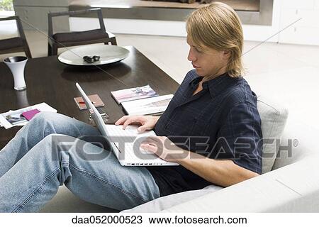Stock Image - Man using laptop computer on sofa. Fotosearch