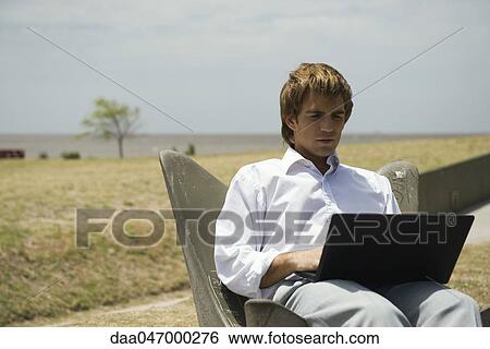 Man using laptop computer outdoors, open field in background View Large Photo Image Stock Photograph - Man using laptop computer outdoors, open field in background. Fotosearch