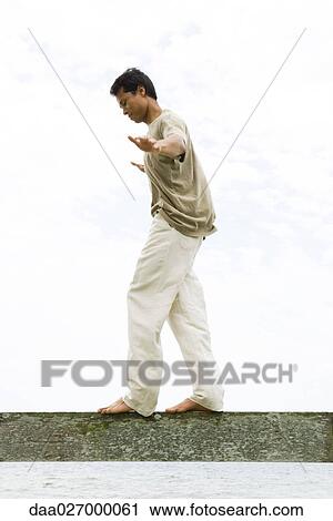 Man walking along guard rail, arms out, looking down, side view View Large Photo Image Stock Image - Man walking along guard rail, arms out, looking down, side view. Fotosearch