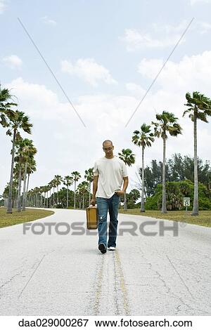 Man walking in center of road, carrying suitcase, looking down View Large Photo Image Stock Photo - Man walking in center of road, carrying suitcase, looking down. Fotosearch