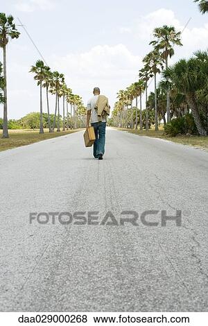 Man walking in center of road, carrying suitcase and jacket, rear view View Large Photo Image Stock Photo - Man walking in center of road, carrying suitcase and jacket, rear view. Fotosearch