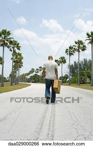 Man walking in center of road, carrying suitcase, rear view View Large Photo Image Stock Photograph - Man walking in center of road, carrying suitcase, rear view. Fotosearch