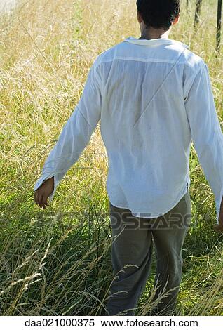 Stock Photography - Man walking through field, rear view. Fotosearch