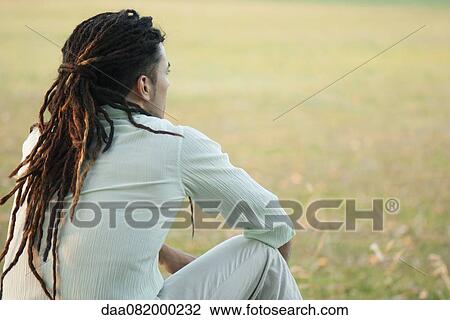 Stock Image - Man with dreadlocks sitting outdoors, rear view. Fotosearch