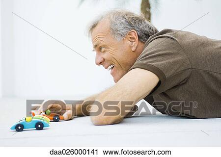 Mature man lying on the ground, playing with toy cars, smiling, side view View Large Photo Image Stock Image - Mature man lying on the ground, playing with toy cars, smiling, side view. Fotosearch
