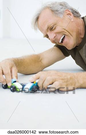 Mature man lying on the ground, playing with toy cars, smiling, close-up View Large Photo Image Stock Image - Mature man lying on the ground, playing with toy cars, smiling, close-up. Fotosearch
