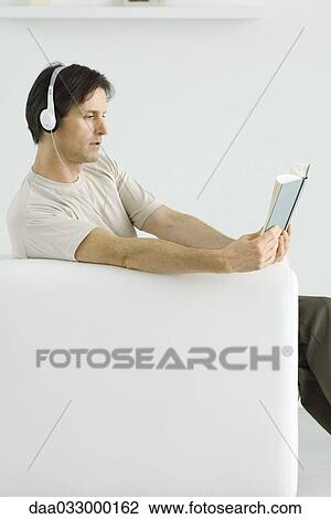 Mature man sitting in armchair, reading book and listening to headphones View Large Photo Image Stock Image - Mature man sitting in armchair, reading book and listening to headphones. Fotosearch