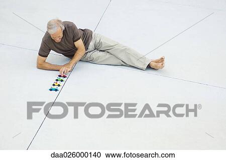 Mature man sitting on the ground, lining up toy cars, high angle view View Large Photo Image Stock Image - Mature man sitting on the ground, lining up toy cars, high angle view. Fotosearch