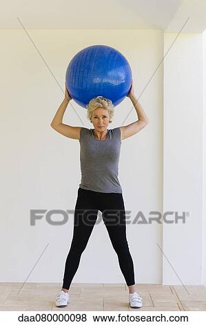 Mature woman holding up fitness ball behind head View Large Photo Image Stock Photo - Mature woman holding up fitness ball behind head. Fotosearch