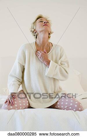 Mature woman kneeling on bed massaging neck View Large Photo Image Stock Photography - Mature woman kneeling on bed massaging neck. Fotosearch
