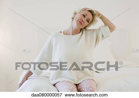 Mature woman kneeling on bed stretching neck View Large Photo Image Stock Photo - Mature woman kneeling on bed stretching neck. Fotosearch