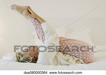 Mature woman lying on bed stretching legs View Large Photo Image Picture - Mature woman lying on bed stretching legs. Fotosearch