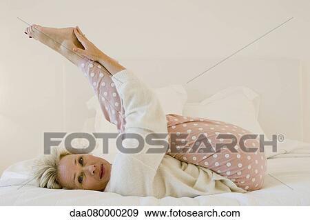 Mature woman lying on bed stretching legs View Large Photo Image Stock Photo - Mature woman lying on bed stretching legs. Fotosearch