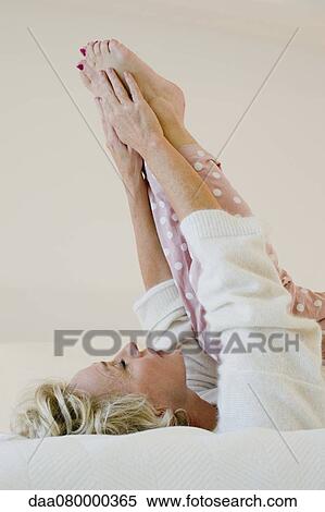 Mature woman lying on bed stretching legs View Large Photo Image Stock Photography - Mature woman lying on bed stretching legs. Fotosearch