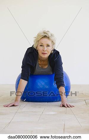 Stock Photograph - Mature woman lying on stomach on fitness ball. Fotosearch