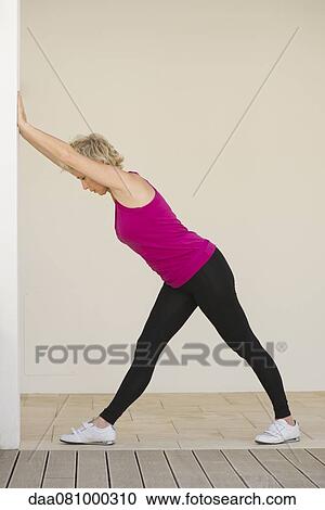 Stock Image - Mature woman pushing against wall, side view. Fotosearch