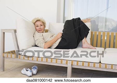 Stock Image - Mature woman reclining on sofa. Fotosearch