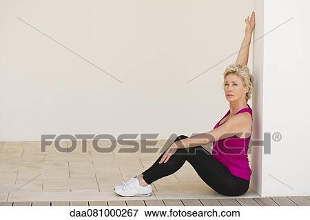 Mature woman sitting against wall, stretching arm View Large Photo Image Stock Photo - Mature woman sitting against wall, stretching arm. Fotosearch