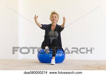 Mature woman sitting on fitness ball with arms out and one leg up View Large Photo Image Picture - Mature woman sitting on fitness ball with arms out and one leg up. Fotosearch